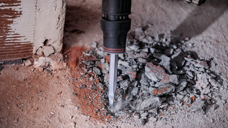 Chisel hammer breaking concrete rubble at the base of a wall.