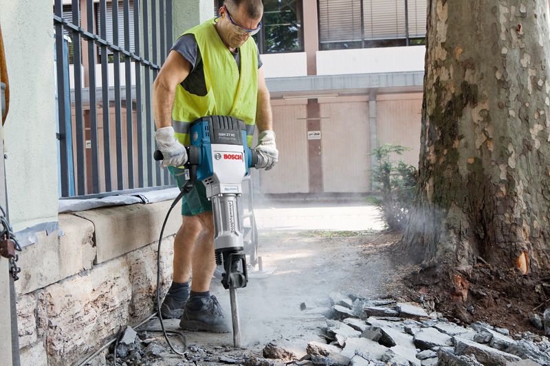 GSH 27 VC A person wearing safety equipment breaks pavement outdoors with a large electric breaker.