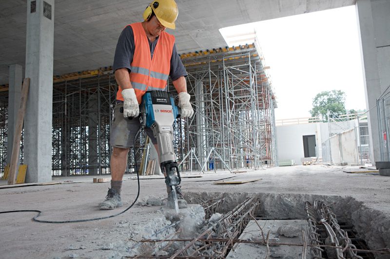 GSH 27 VC A person wearing safety equipment uses a breaker to demolish concrete at a construction site.