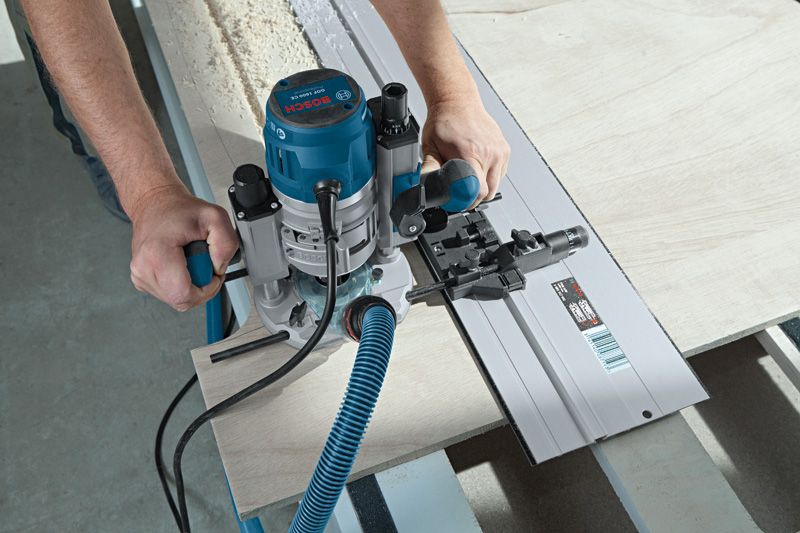 GOF 1600 CE A person uses a blue router to cut wood along a straight guide rail.