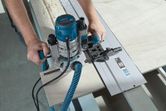 A person uses a blue router to cut wood along a straight guide rail.