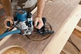A person uses a router to cut a circular hole in a wooden board.