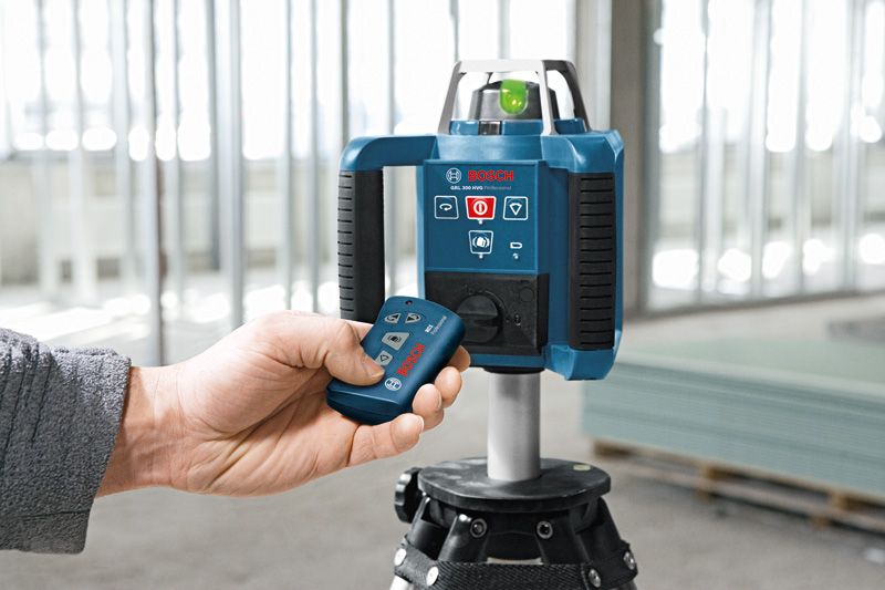 A person operates a laser leveling tool on a tripod inside a construction site.