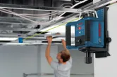 Laser leveling tool projecting a green line as a person installs a suspended ceiling.
