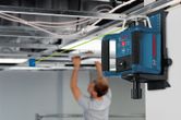 Laser leveling tool projects a green line as a person installs ceiling panels.