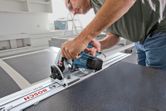 A person wearing safety equipment uses a plunge saw to cut a straight line in a panel.