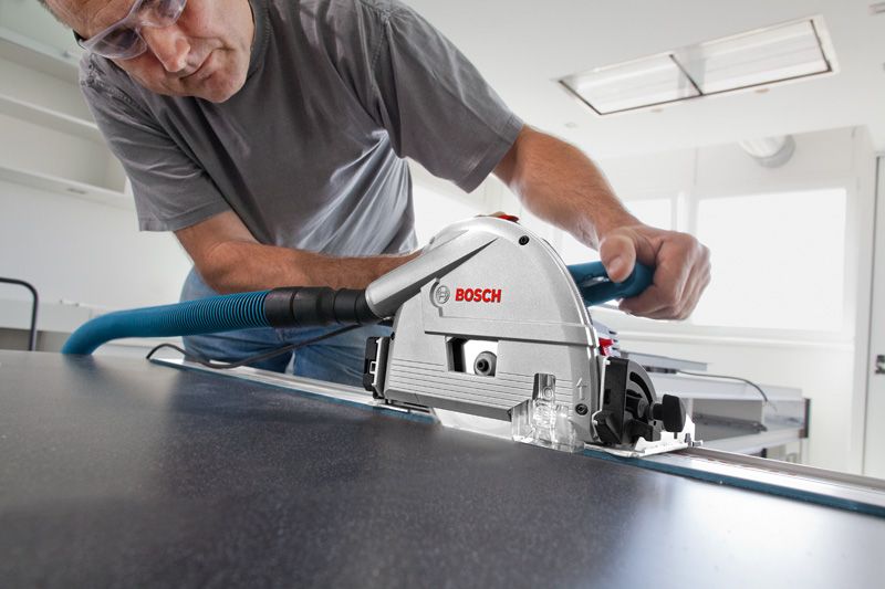 A person wearing safety equipment cuts a panel with a plunge saw attached to a guide rail.