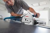 A person wearing safety equipment cuts a panel with a plunge saw attached to a guide rail.